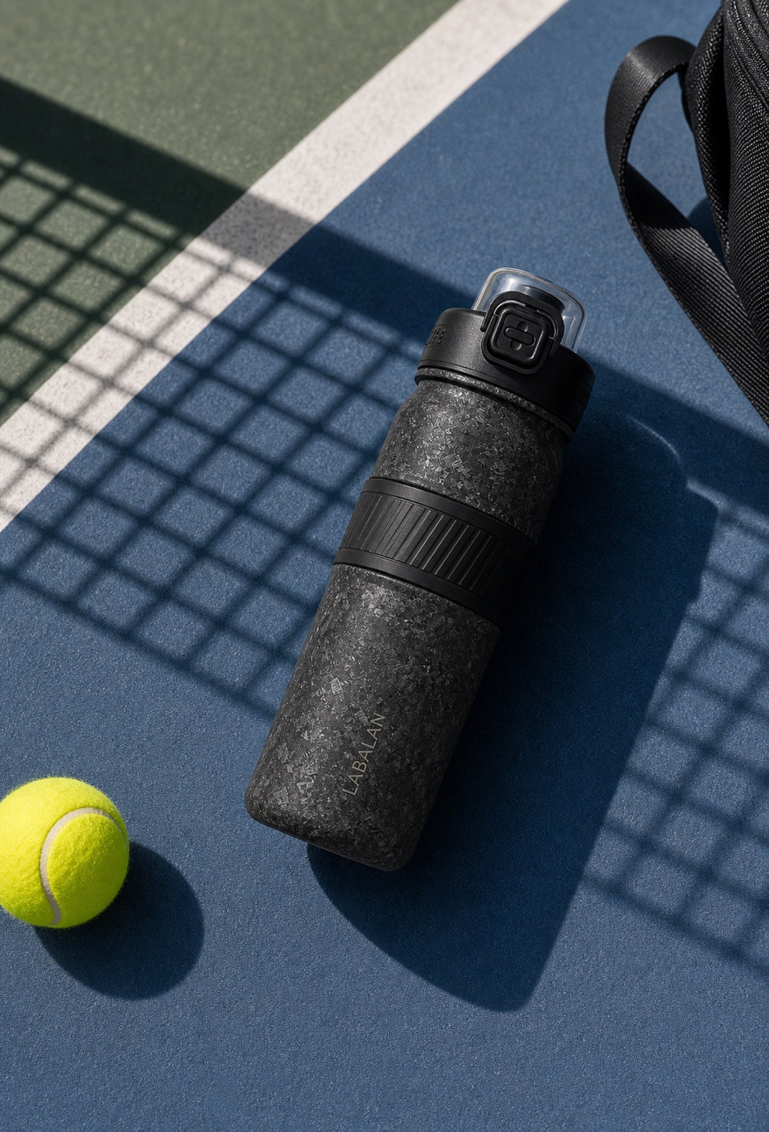 Black LABALAN Titanium Sport Water Bottle on a blue and green tennis court